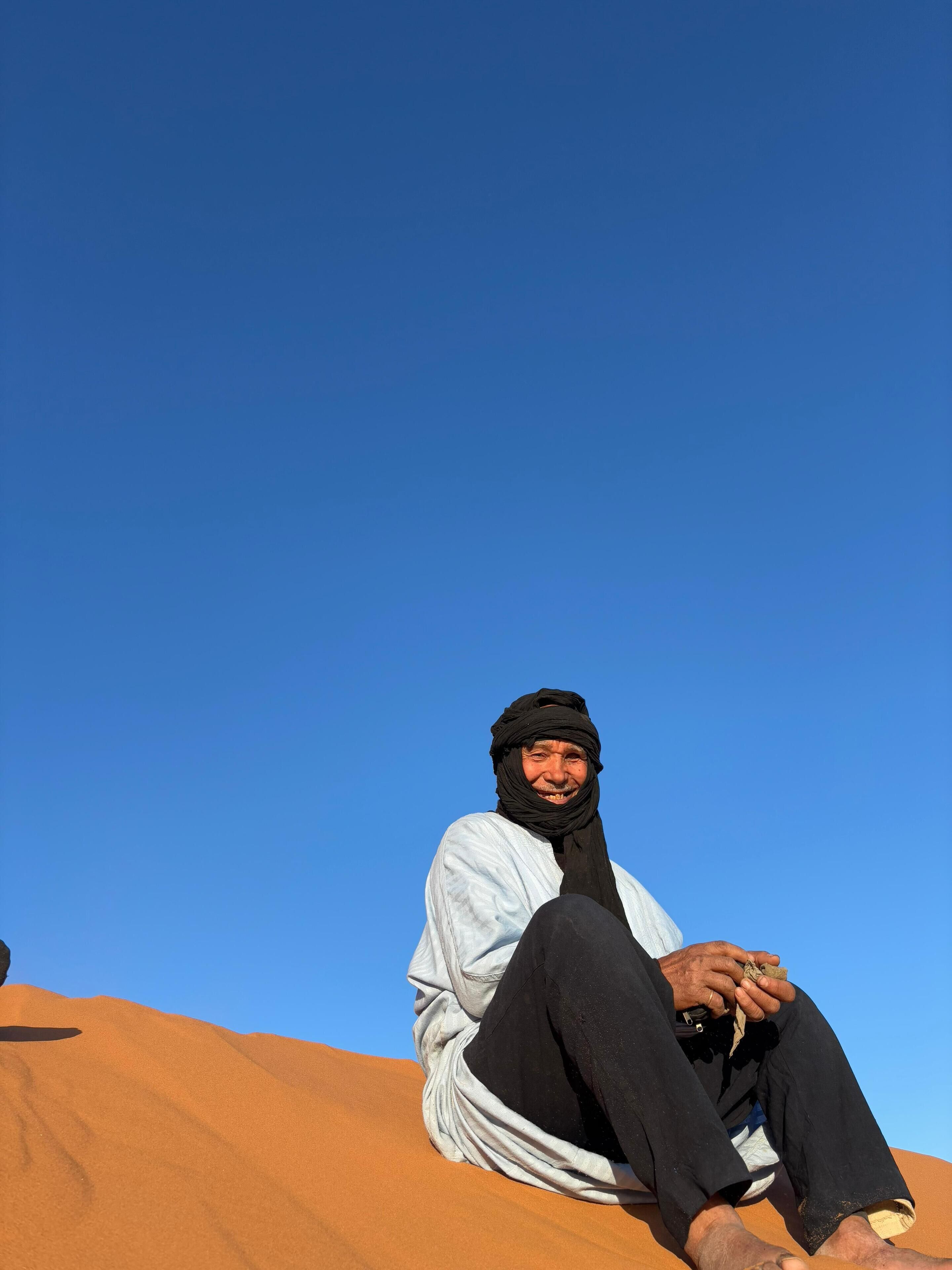 A person sitting on a sand dune with a clear blue sky in the background.
