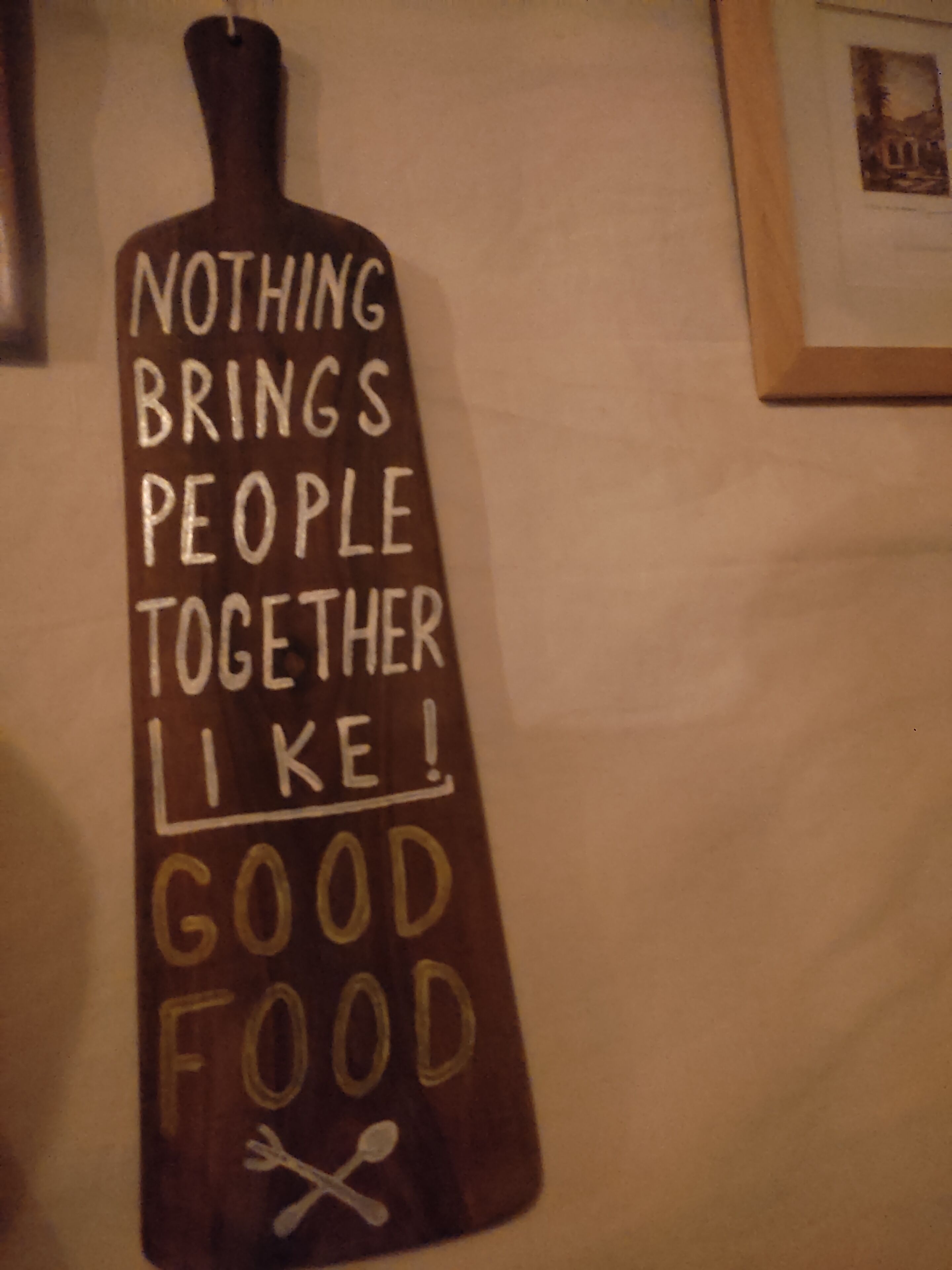A wall with a wooden sign that reads "NOTHING BRINGS PEOPLE TOGETHER LIKE GOOD FOOD."