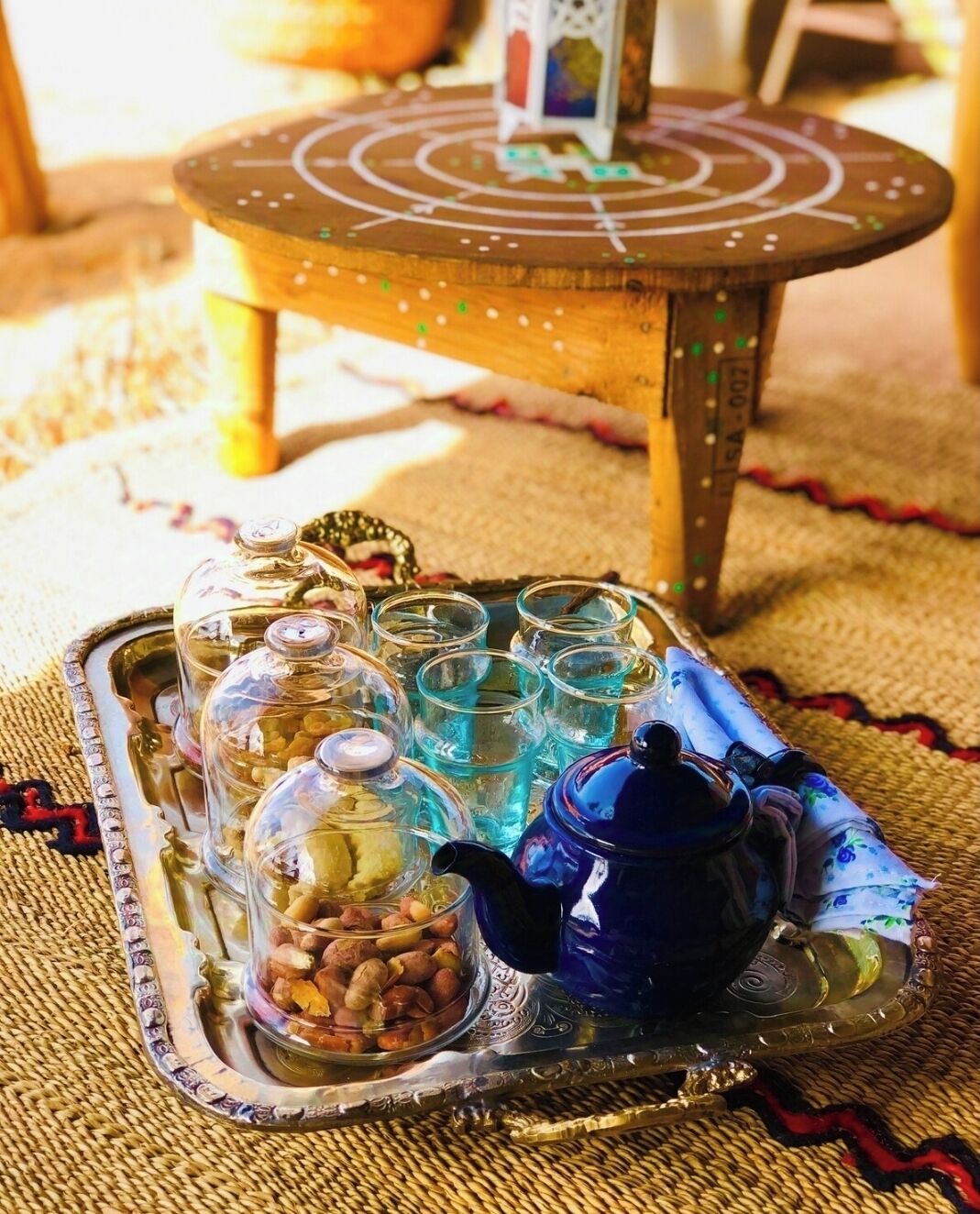 A tray with a teapot and glasses, a jar of nuts, and a small table with a decorative item in the background.
