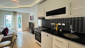 Une cuisine moderne avec des meubles blancs, un plan de travail noir et un crédence en carreaux noirs. On y trouve un coin repas avec un canapé et des chaises, ainsi qu’un téléviseur posé sur un meuble.