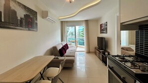 Un salon moderne comprenant un canapé, une table à manger, des chaises, un téléviseur et un coin cuisine avec une cuisinière.