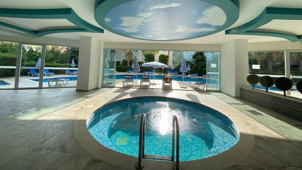 Une piscine intérieure avec des parois en verre transparent, des chaises longues bleues et des parasols.