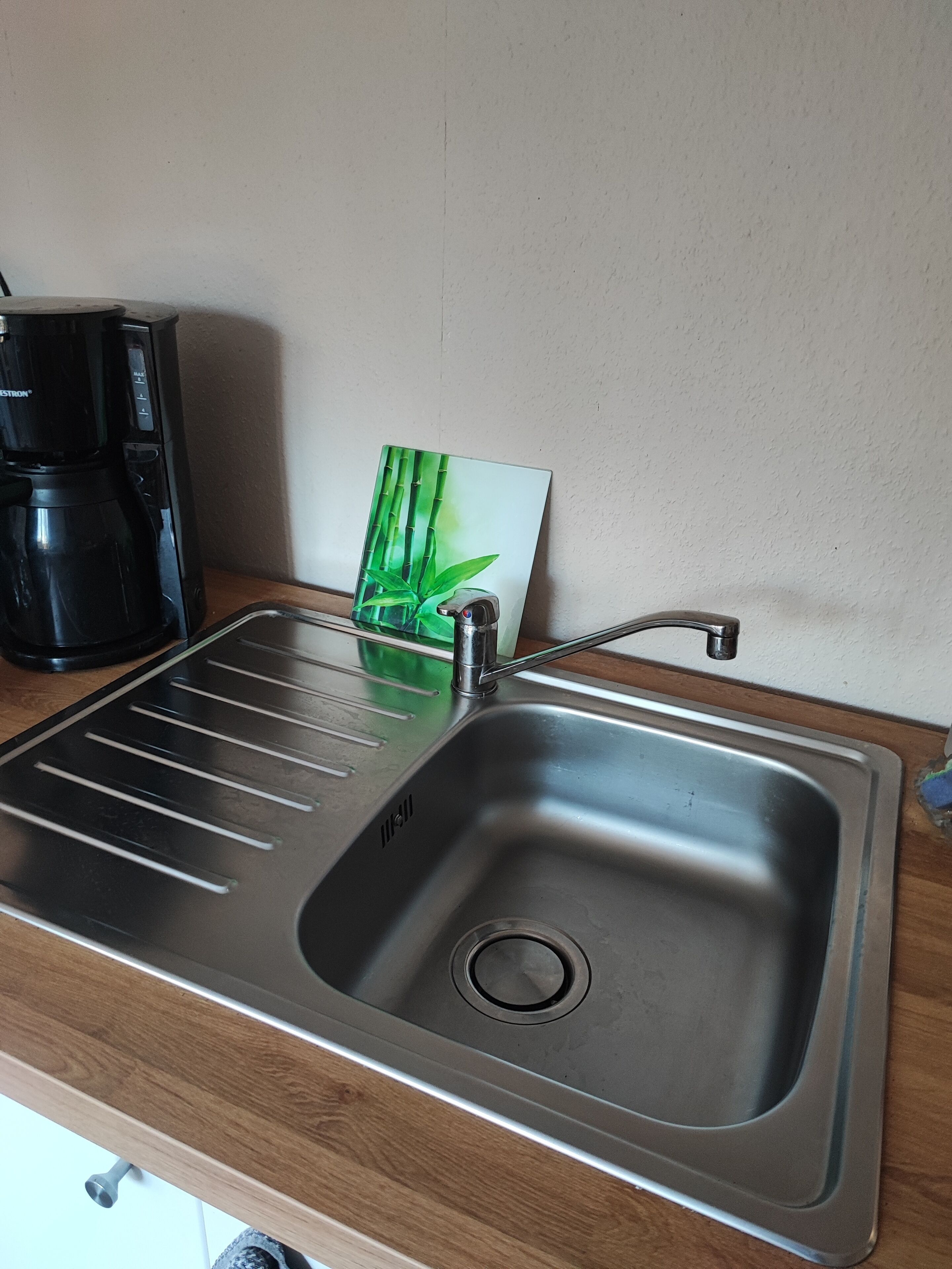 Un évier de cuisine en acier inoxydable avec un seul robinet, une machine à café et une carte décorée de motifs en bambou posée sur le comptoir.