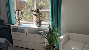 Une pièce avec une fenêtre, un canapé blanc, un bureau avec un ordinateur et une plante en pot.