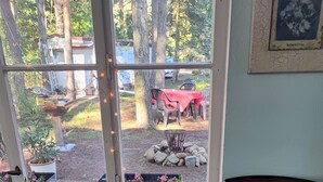 Une pièce dotée d’une grande fenêtre donnant sur une zone boisée, avec une plante en pot, une chaise et une table recouverte d’une nappe rouge.