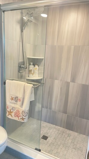 Een douchecabine met glazen wanden, een handdouche, een glazen deur en een handdoek met zeediermotieven aan de deur.