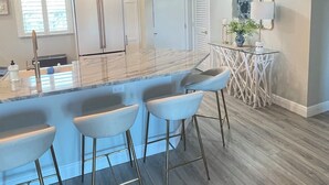 A modern kitchen with a marble island, bar stools, pendant lights, and a refrigerator. - 2-bedroom Condo in lovely Siesta Key Beach minimum 1 Month 55 & over Second Unit (Sarasota)