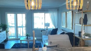A modern kitchen with white cabinets, a sink, and a countertop. There are two hanging pendant lights and a large window with curtains. - 2-bedroom Condo in lovely Siesta Key Beach minimum 1 Month 55 & over Second Unit (Sarasota)