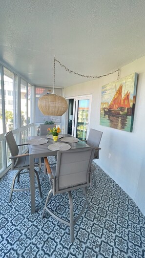Een eethoek met een tafel voor vier personen, omringd door stoelen, een hanglamp en een schilderij aan de muur.