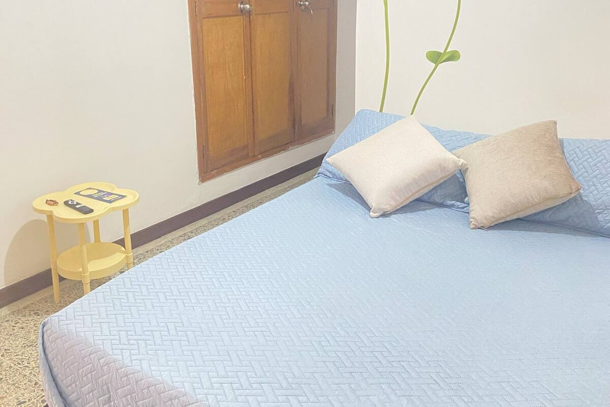 Un dormitorio con cama, almohadas, una mesita y una pared decorada con un diseño floral.