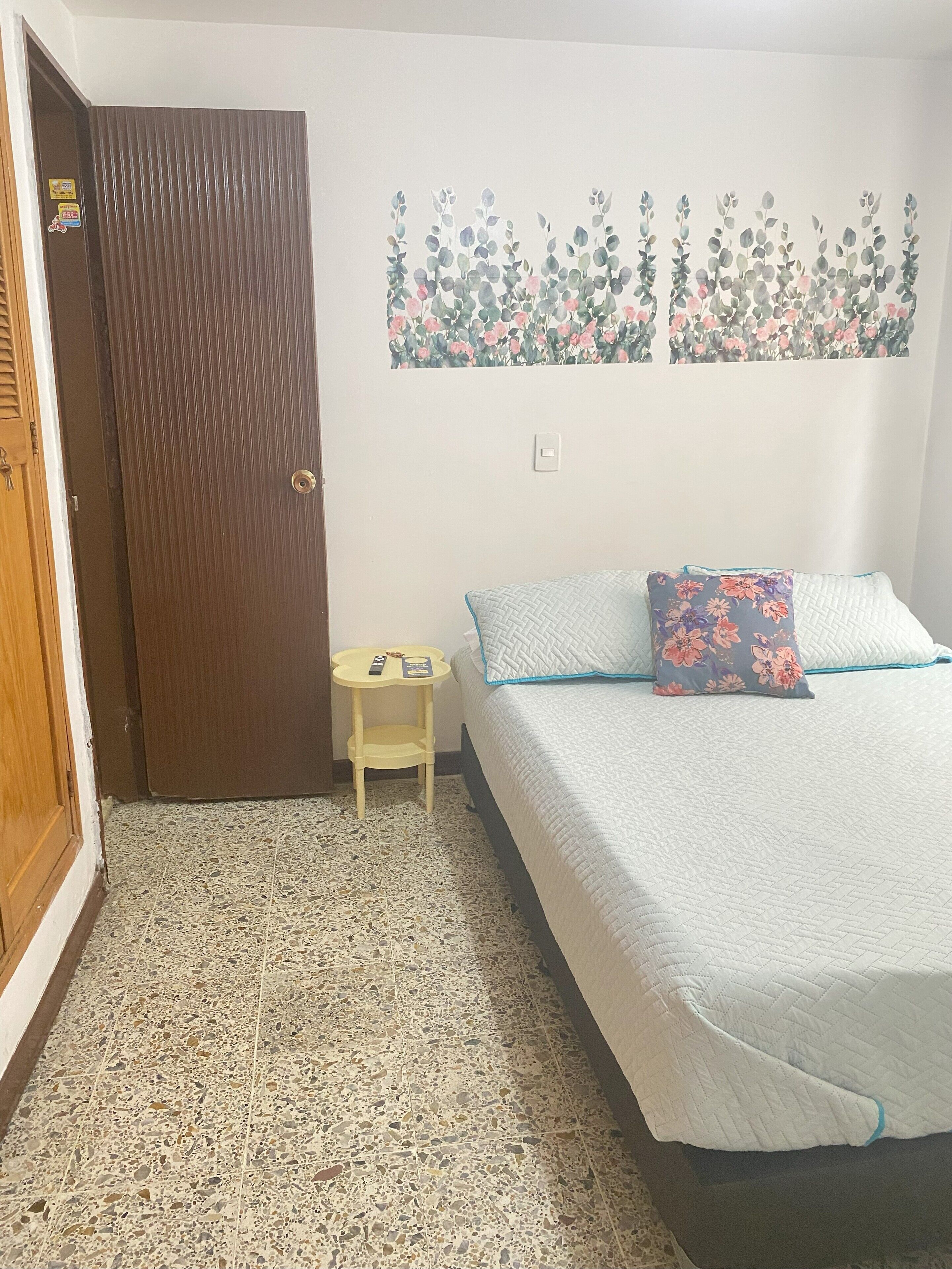 Un dormitorio con cama, una mesita de noche, una puerta y un adorno en la pared.