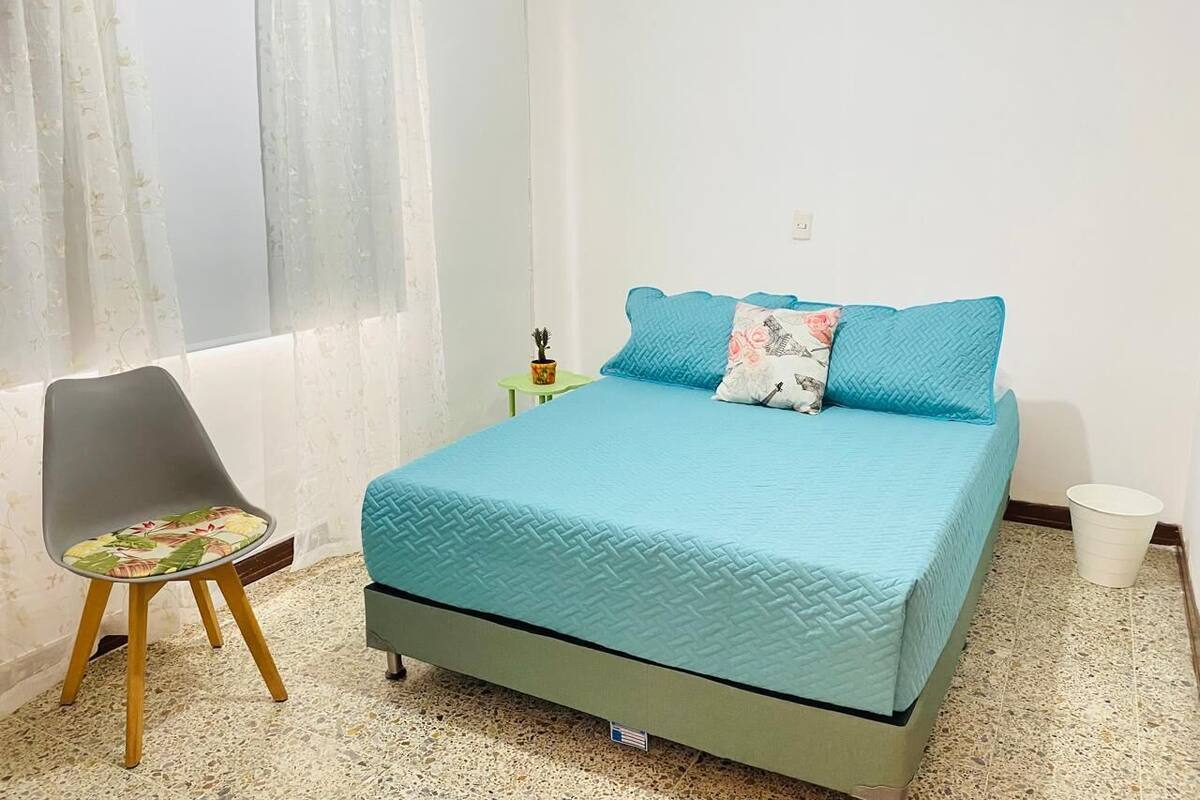 Un dormitorio con una cama, una silla, una mesita y una planta en maceta.