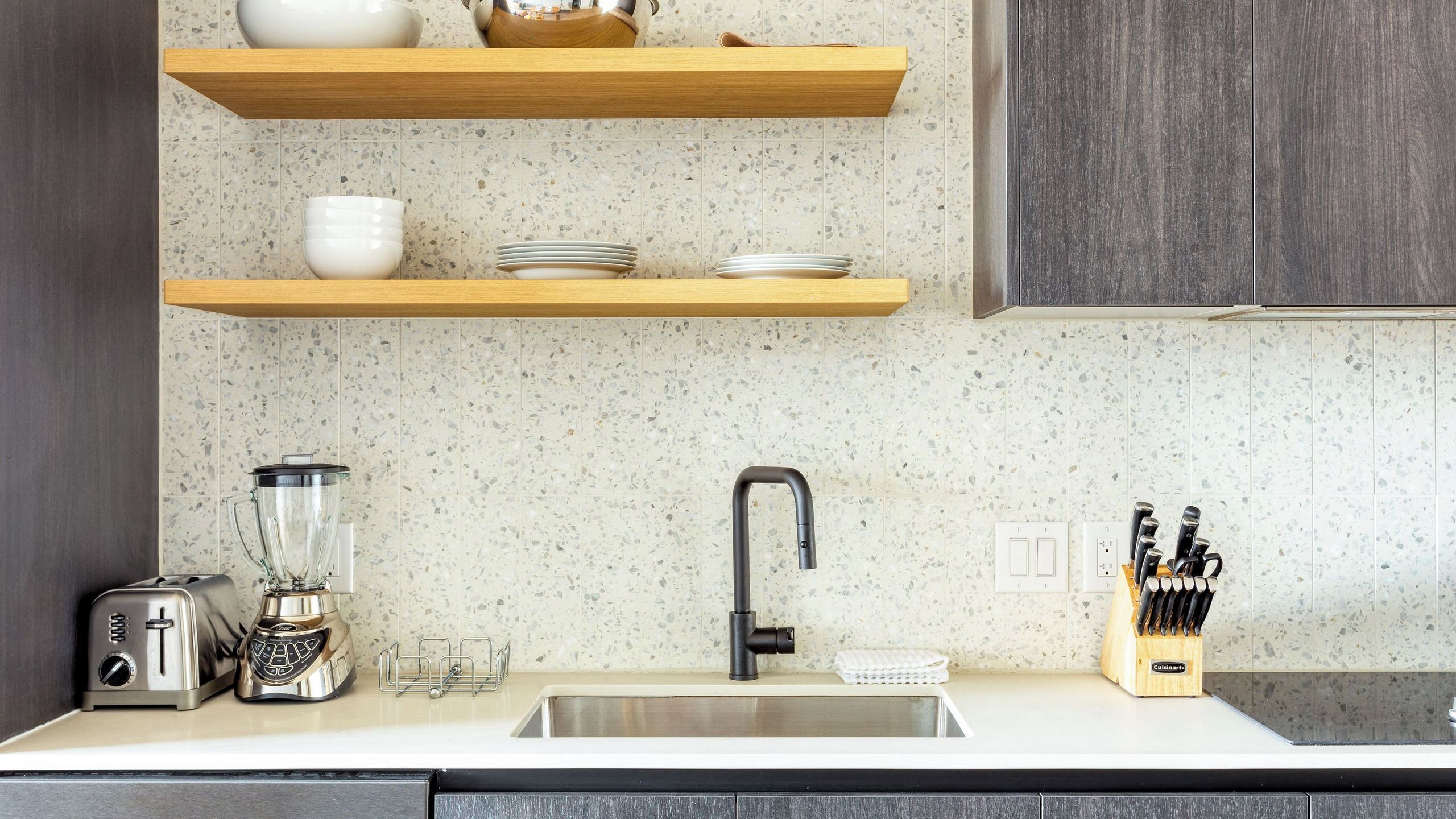 A kitchen with granite countertops, a stainless steel sink, a built-in knife block, and a coffee maker.