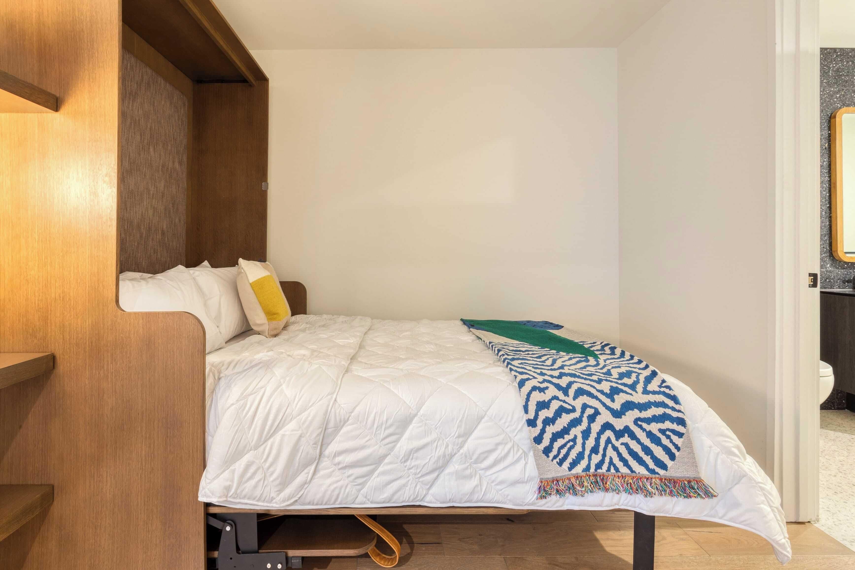 A compact bedroom with a bed, a wooden headboard, and a small shelf.