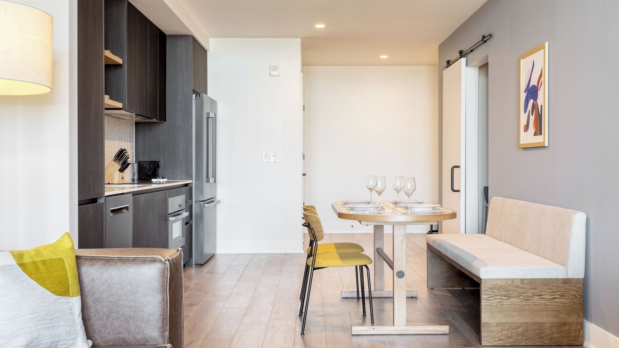 A modern kitchen with dark cabinets, a refrigerator, and a dining area with a table and chairs.