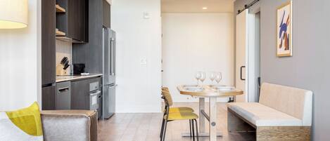 A modern kitchen with dark cabinets, a refrigerator, and a dining area with a table and chairs.