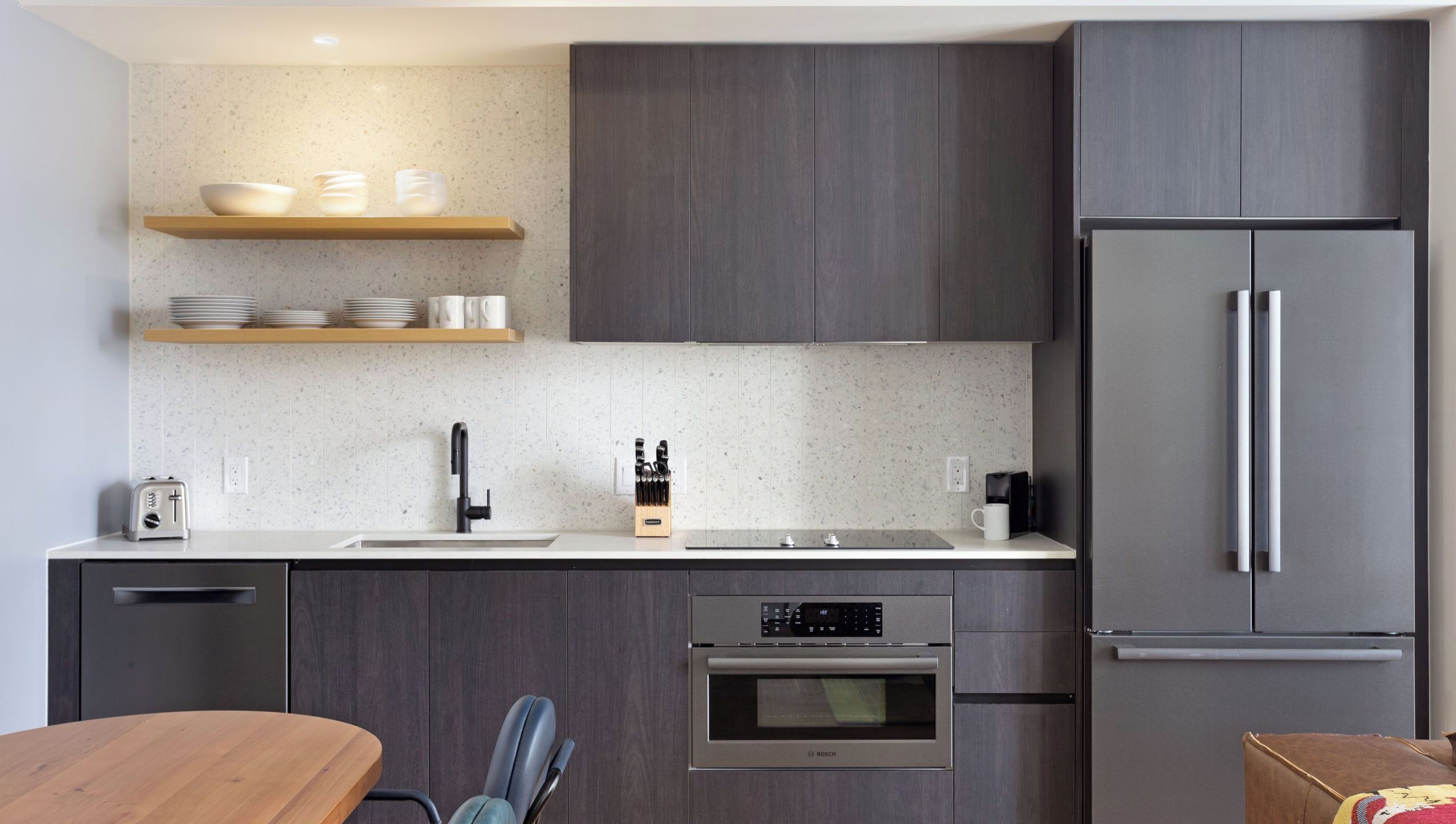 A modern kitchen with a built-in oven, a refrigerator, and a wooden dining table.