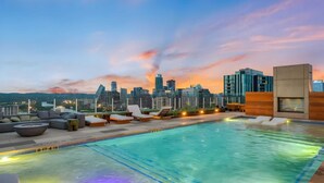Une piscine sur le toit, dotée de chaises longues et offrant une vue sur les toits de la ville au crépuscule.