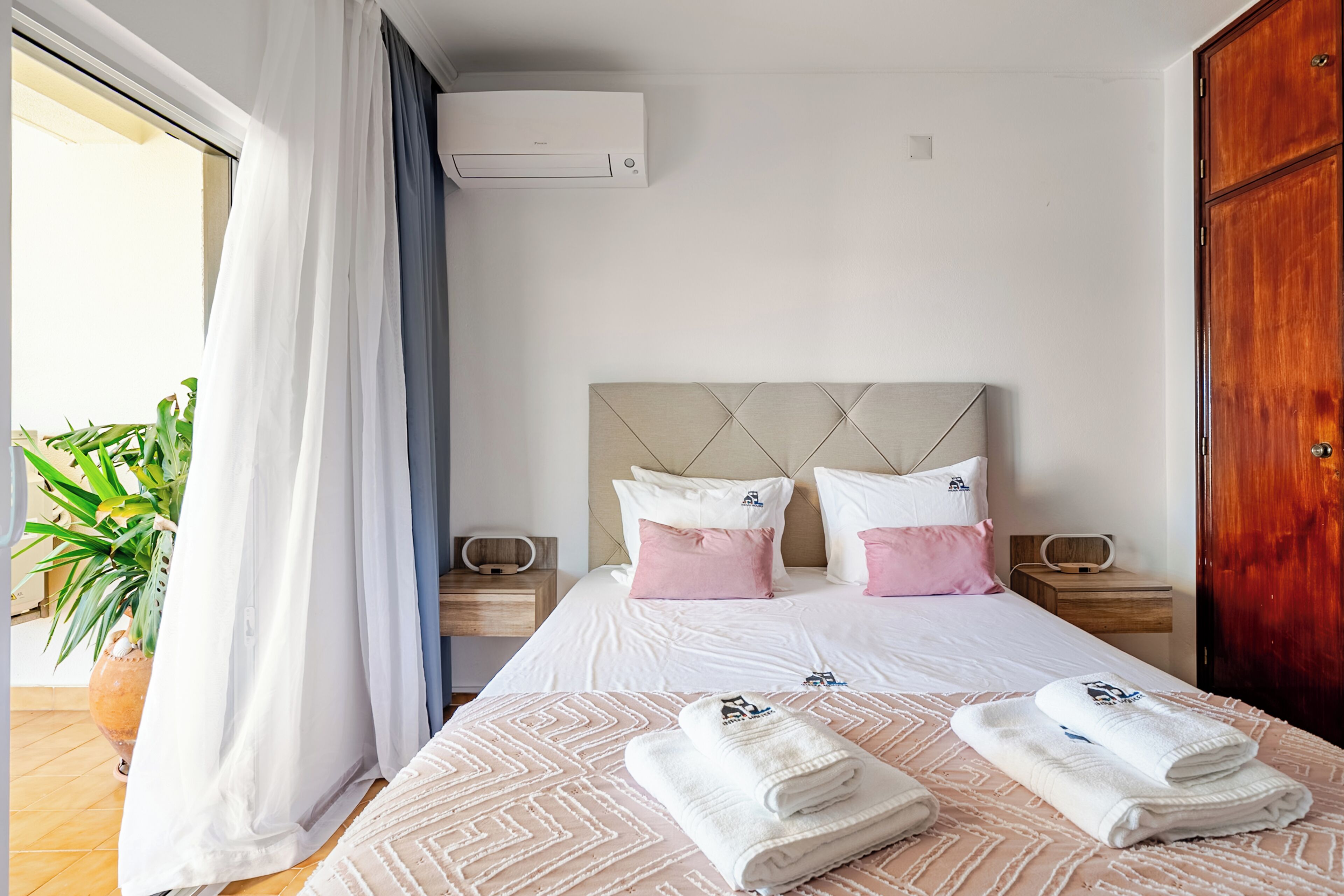 Ein Hotelzimmer mit Bett, zwei Nachttischen, einem Kopfteil, einer Klimaanlage, einer Tür und einer Topfpflanze.