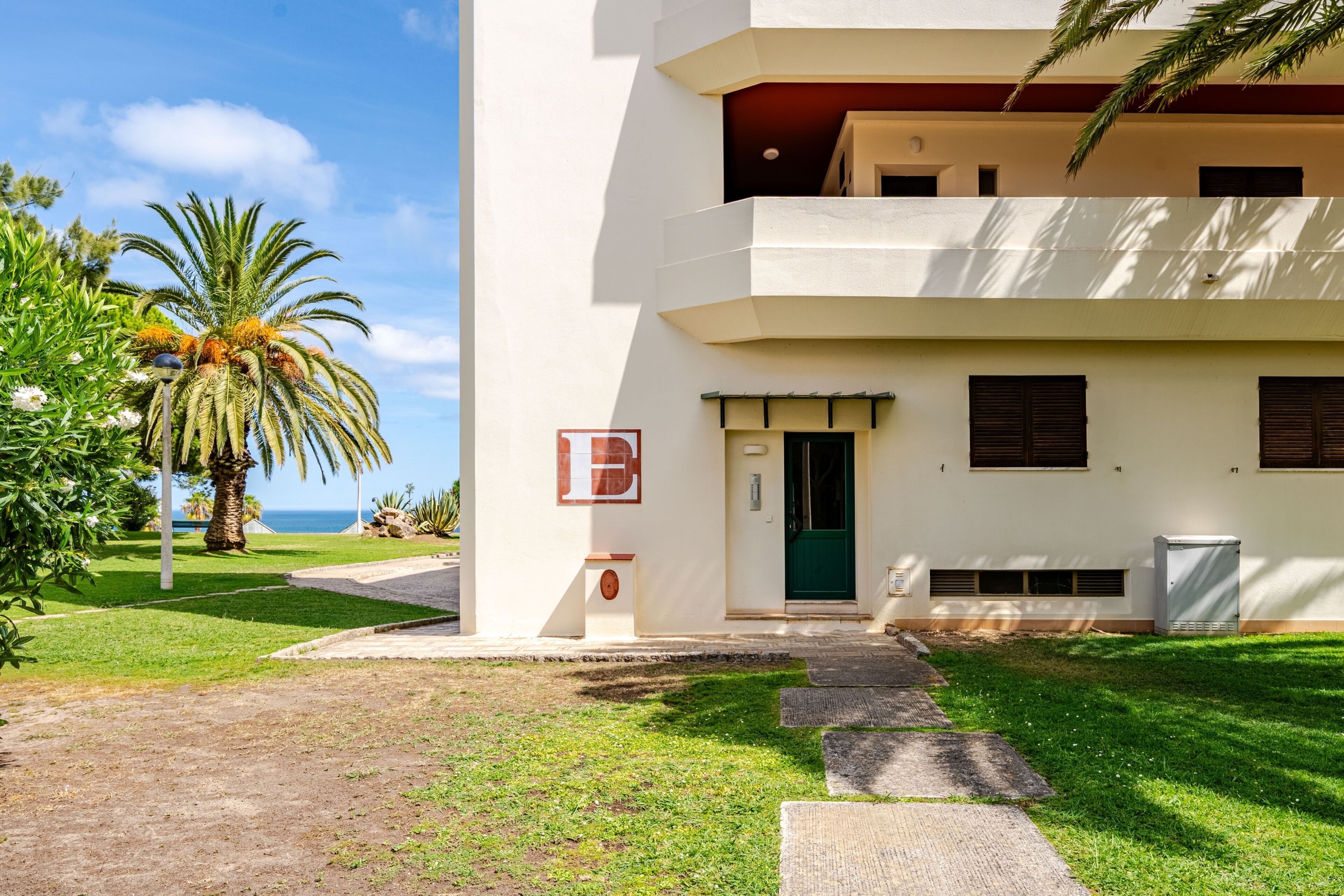 A two-story building with a green door, a small outdoor seating area, and a palm tree in the foreground.