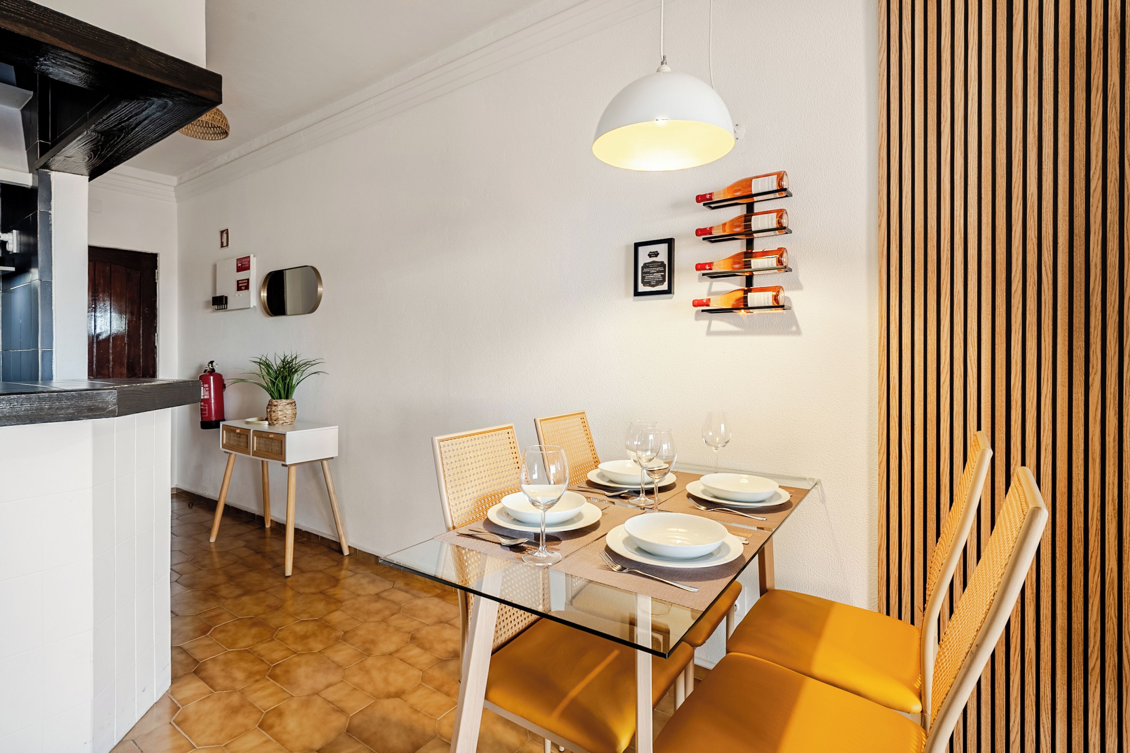 A dining area with a glass table, wooden chairs, and a hanging light fixture.