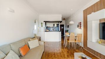 Een moderne woonkamer met een bank, een eethoek met stoelen en een keuken op de achtergrond.