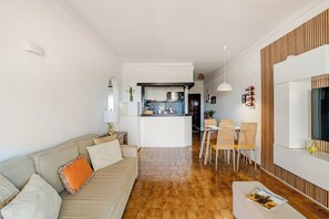 Un salon moderne avec un canapé, un coin repas avec des chaises et une cuisine en arrière-plan.