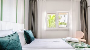 Une chambre d’hôtel avec un lit, des oreillers, une chaise et une fenêtre avec des rideaux.