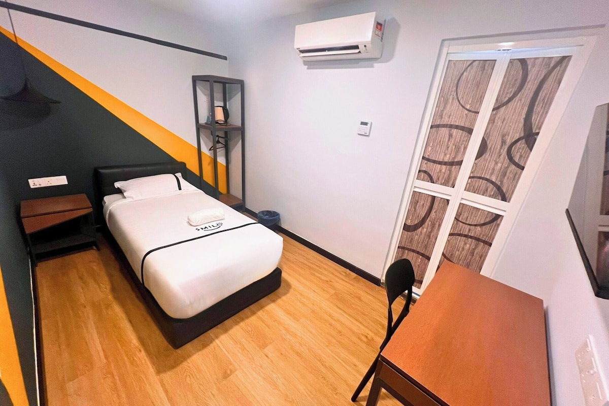 Une chambre d’hôtel équipée d’un lit, d’un bureau, d’un climatiseur et d’une fenêtre avec un rideau à motifs.