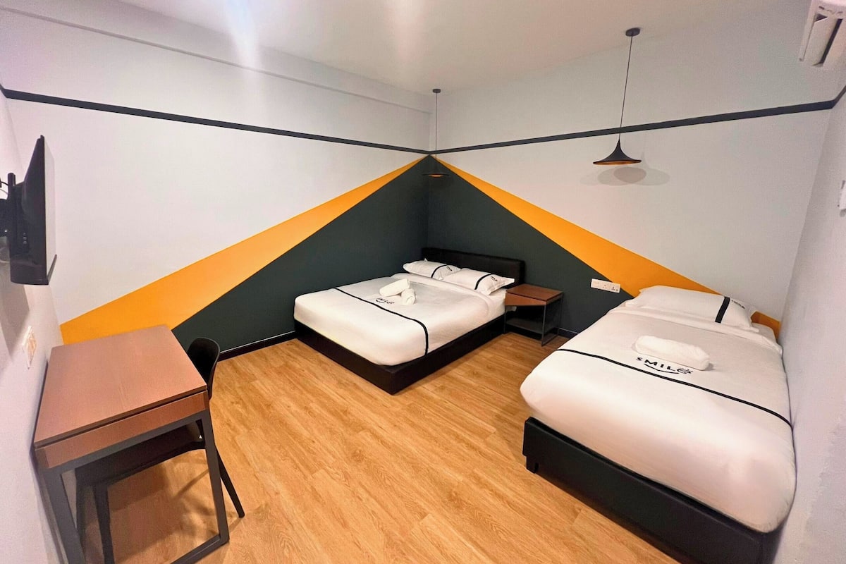 Une petite pièce triangulaire comprenant deux lits, un bureau et une chaise.