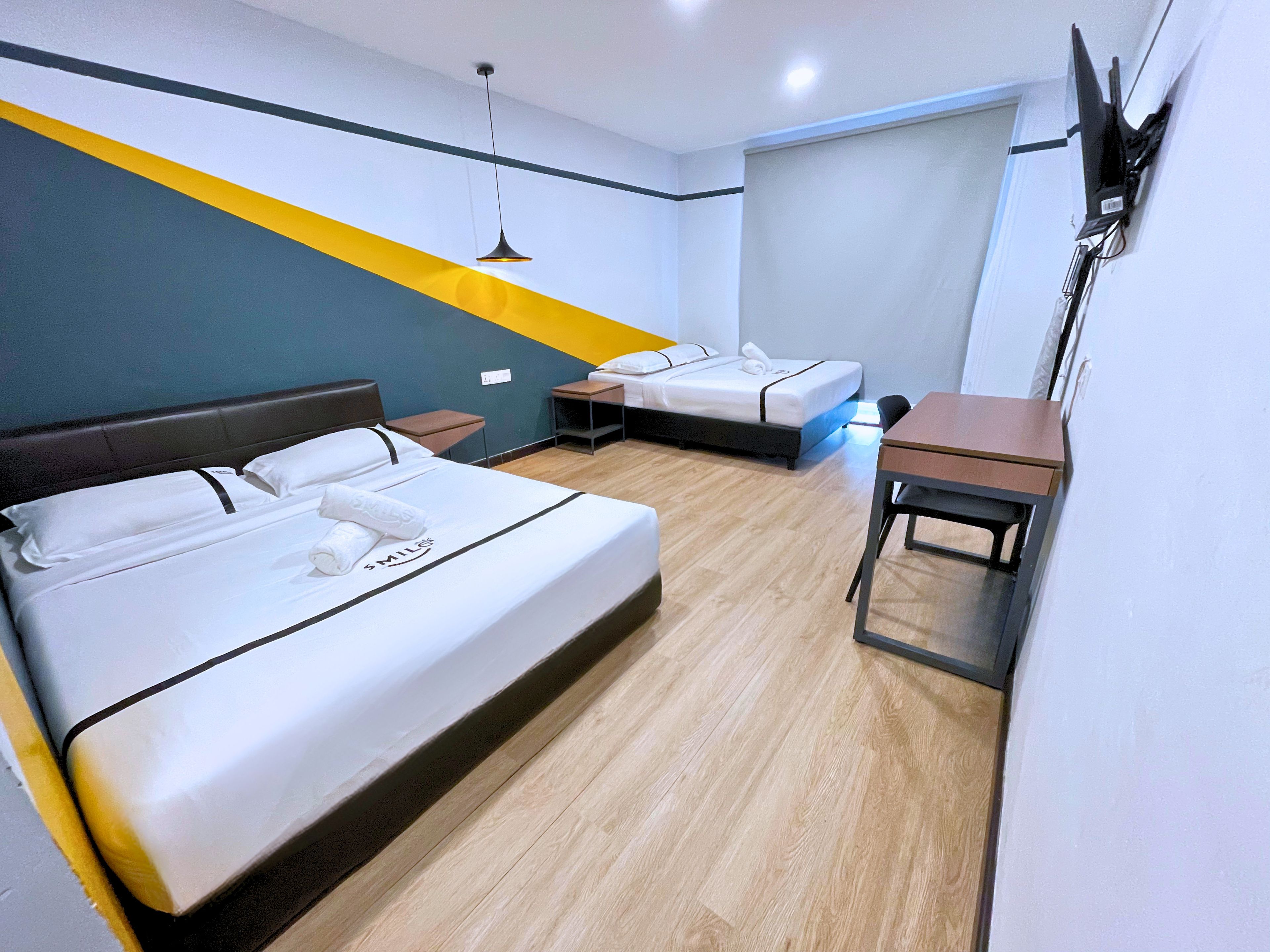 A hotel room with two beds, a desk, and a TV mounted on the wall.