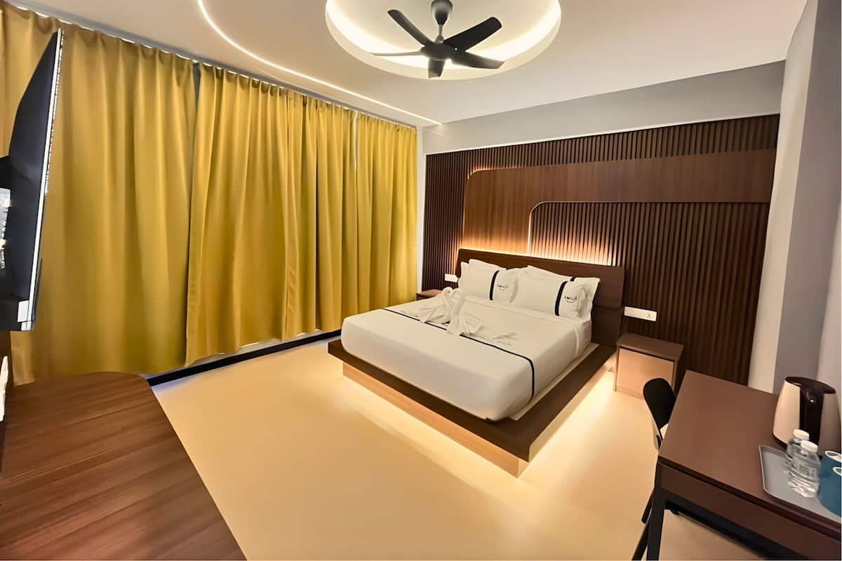 Une chambre d’hôtel moderne dotée d’un grand lit, d’un bureau, d’un ventilateur de plafond et d’une grande fenêtre avec des rideaux.