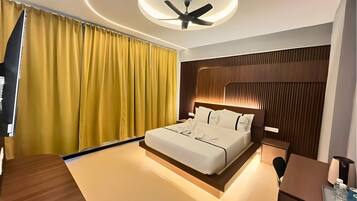 A modern hotel room with a large bed, a desk, a ceiling fan, and a large window with curtains.