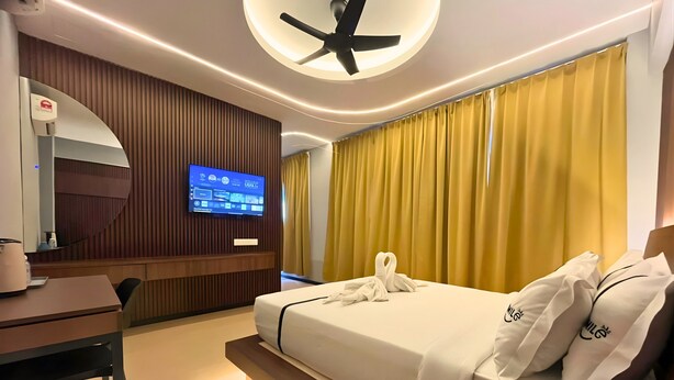 Quarto de hotel moderno com cama, escrivaninha, cadeira, televisão fixada na parede e ventoinha de teto.
