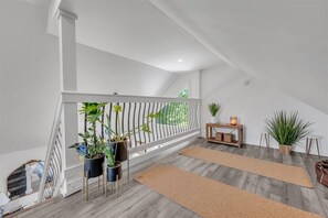 Experience the airy loft with a high ceiling, white railing, and potted plants, perfect for a cozy retreat.