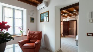 Un salón amplio con un sillón de cuero, un ventanal con cortinas, un equipo de aire acondicionado y un techo de madera.