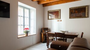 A living room with a wooden ceiling, a dining table with chairs, a sofa, a window with curtains, and two framed pictures on the wall. - Varenna Vintage by Wonderful Italy (Perledo)
