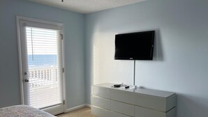 Une chambre à coucher avec un lit, une commode, un téléviseur fixé au mur et une porte avec des stores.