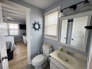 A bathroom with a toilet, sink, and vanity. There is a ceiling fan, a wall-mounted light fixture, and a window with blinds. - NEWLY RENOVATED Canalfront w/ Boat Dock & Close to the Beach by Williamson Realt (Ocean Isle Beach)