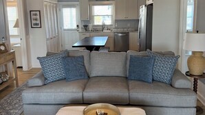 Ein modernes Wohnzimmer mit grauem Sofa, Couchtisch und einer Küche im Hintergrund.
