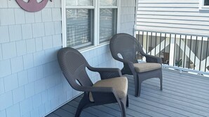 Une véranda couverte avec deux fauteuils en osier, une grande décoration en forme d’ancre et une fenêtre avec des stores.