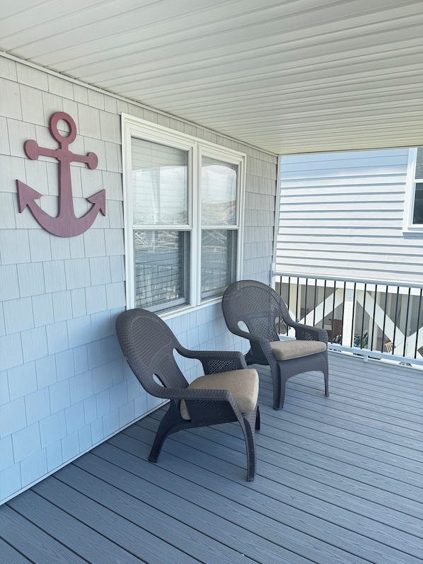 A covered porch with two wicker chairs, a large anchor decoration, and a window with blinds. - NEWLY RENOVATED Canalfront w/ Boat Dock & Close to the Beach by Williamson Realt (Ocean Isle Beach)