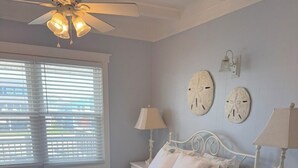 Une chambre à coucher avec un lit, des tables de chevet, des horloges murales et un ventilateur de plafond.