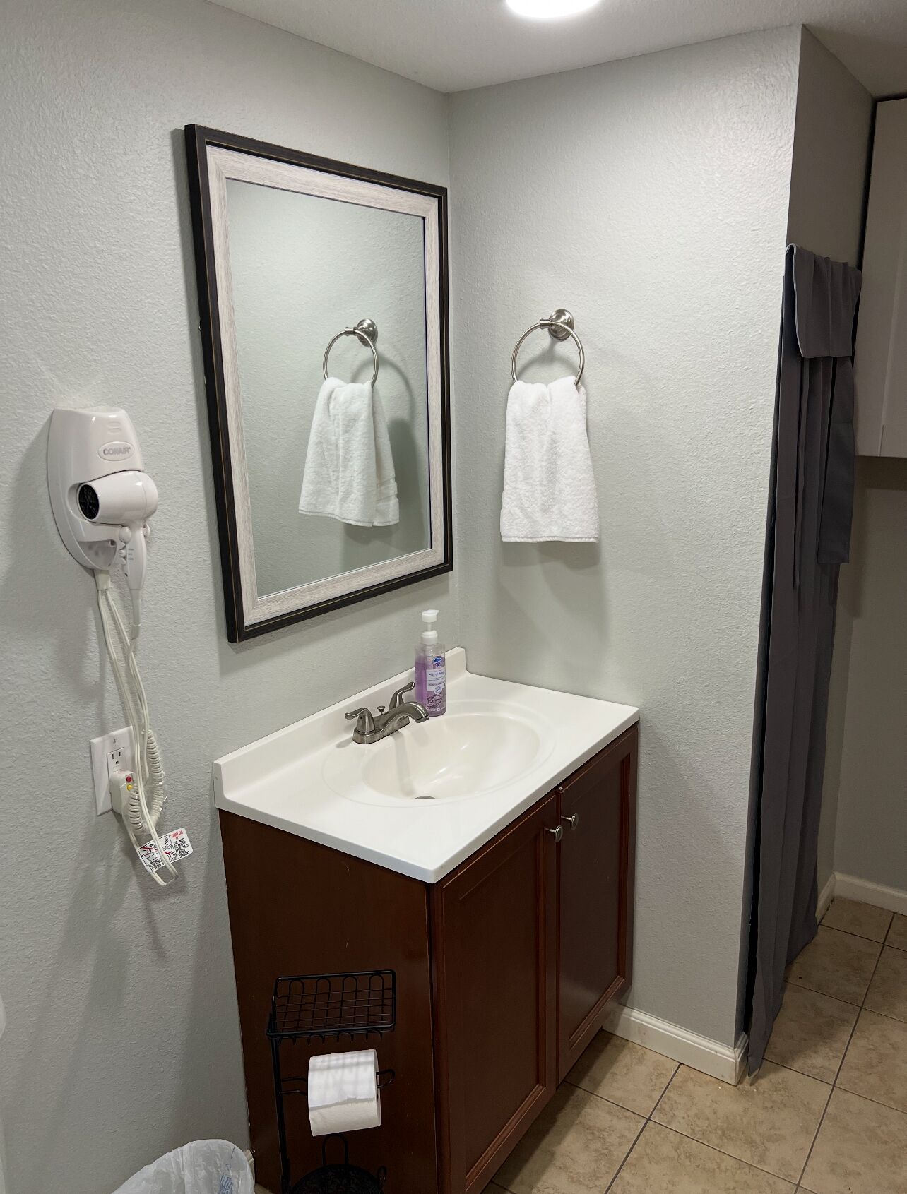 A bathroom with a white sink, a mirror, a towel rack, a hand dryer, and a toilet paper holder.