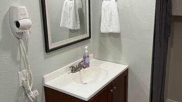 A bathroom with a white sink, a mirror, a towel rack, a hand dryer, and a toilet paper holder.