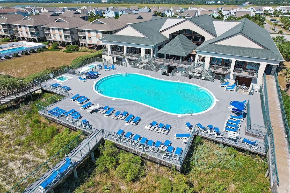 A resort with a large swimming pool surrounded by lounge chairs, a deck area, and multiple buildings with balconies.