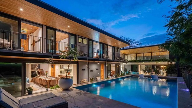 Ein modernes, zweistöckiges Haus mit Swimmingpool, Sitzgelegenheiten im Freien und Essbereich.