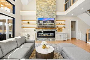 A modern living room with a stone fireplace, grey sofas, and a flat-screen TV.