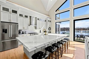Een moderne keuken met een ruim kookeiland, roestvrijstalen apparatuur en uitzicht op een waterpartij door grote ramen.
