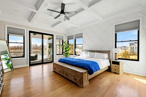 A bedroom with a bed, a ceiling fan, a nightstand, a dresser, and large windows. - Serene Lakefront Lake Anna, Beach, Dock, Pool (Louisa County)